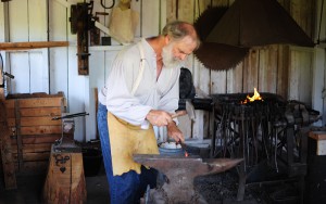 blacksmithing volunteer works at an anvil